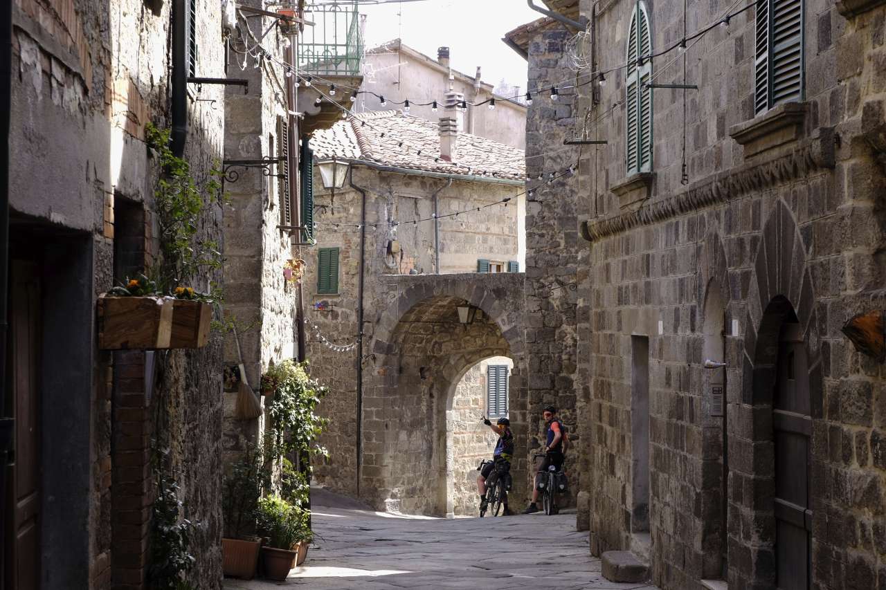 Two gravel bikers in a small alley in the historical center of Abbadia San Salvatore