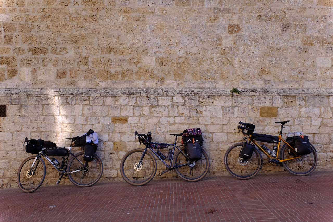 Three packed gravel bikes leaning on a historic wall in Tuscany