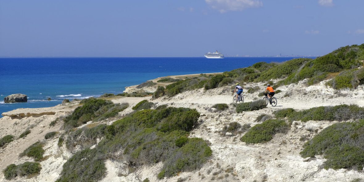 Two gravel bikers in front of a Mediterranean panorama on the coast of Cyprus.