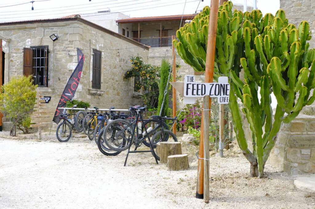 Feed Zone Cafe, a bike stop in Tochni, Cyprus. You can see gravel bikes lined up, a historic building and a large cactus.