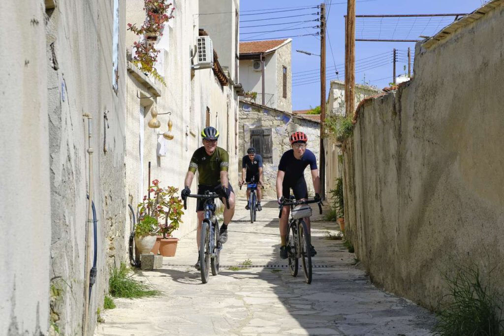 Three gravel bikers ride through a narrow alley in Choirokoitia on Cyprus