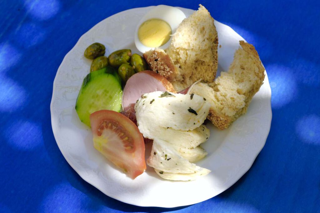 Plate with Cypriot snacks: fresh goat halloumi, freshly baked bread, tomato, cucumber, sausage of Cyprus, egg, pickled snack
